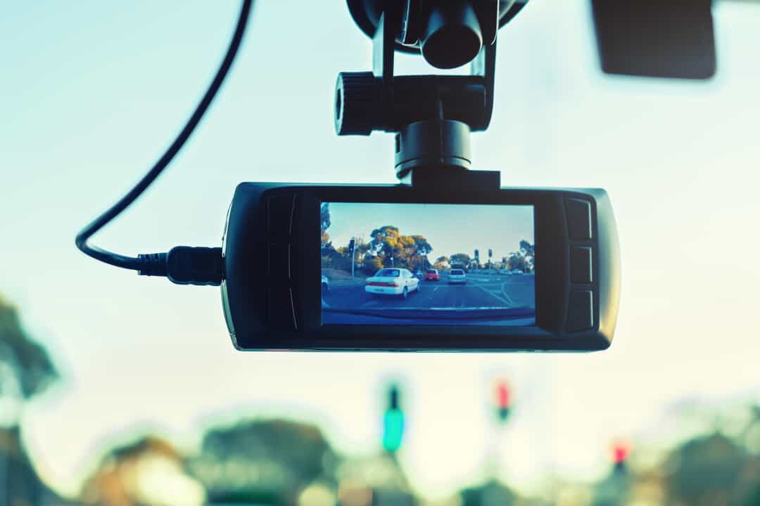 Close up of a dashboard camera mounted on a car's windshield with cars on the street in view